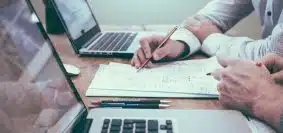 person holding pencil near laptop computer