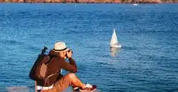 man sitting on dock taking photo of sea