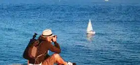 man sitting on dock taking photo of sea